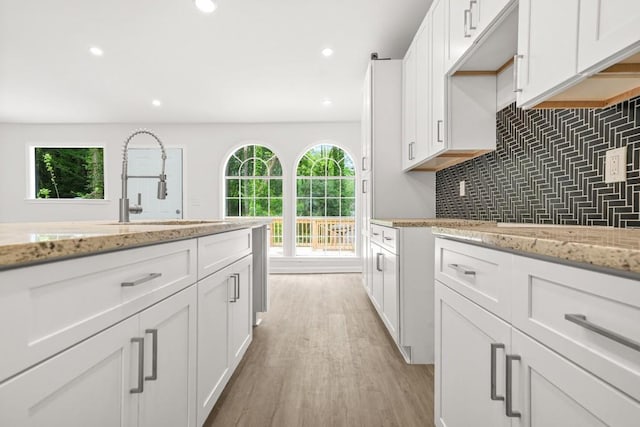 kitchen featuring light wood-type flooring, white cabinets, a wealth of natural light, and tasteful backsplash