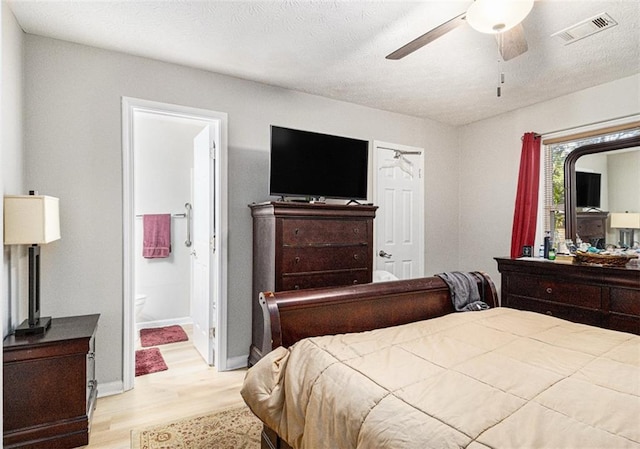 bedroom featuring ceiling fan, ensuite bathroom, a textured ceiling, and light wood-type flooring