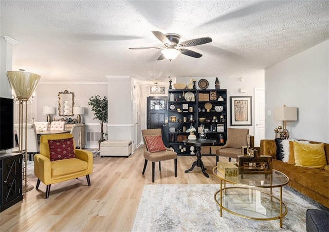 living room with a textured ceiling, ornamental molding, ceiling fan, and light wood-type flooring