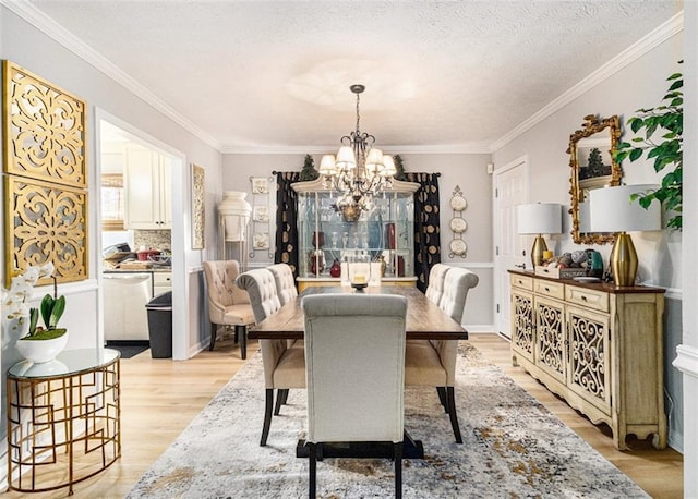 dining room with an inviting chandelier, ornamental molding, light hardwood / wood-style flooring, and a textured ceiling