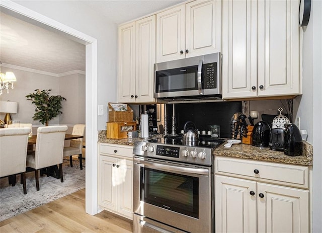 kitchen with dark stone countertops, stainless steel appliances, ornamental molding, a chandelier, and light wood-type flooring