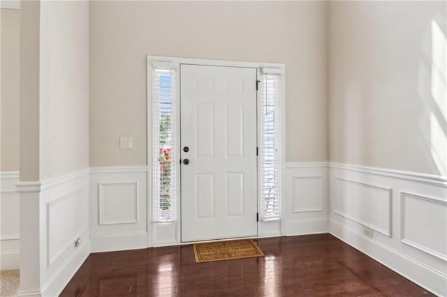 foyer entrance with dark wood-type flooring, a decorative wall, and a wainscoted wall