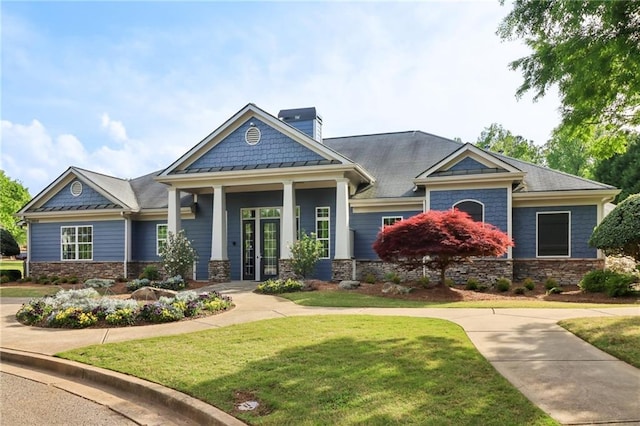 craftsman inspired home featuring a standing seam roof, stone siding, a chimney, and a front yard