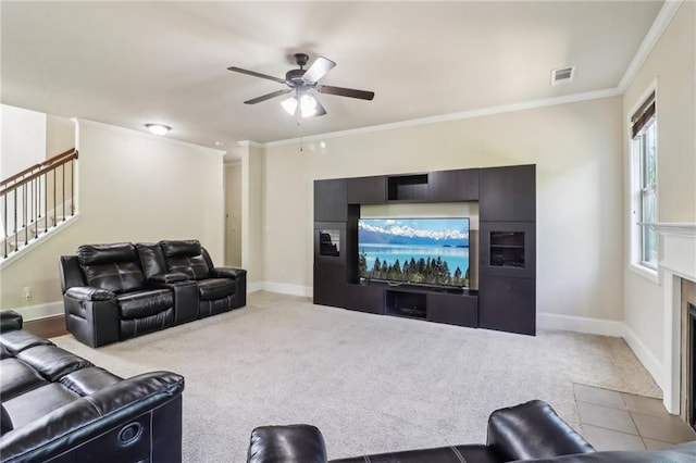 carpeted living room with visible vents, crown molding, stairs, a fireplace with flush hearth, and a ceiling fan