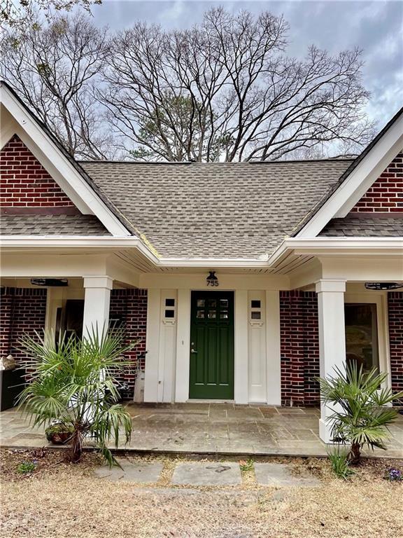 doorway to property featuring a porch, brick siding, and a shingled roof