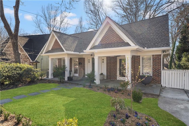 view of front of home featuring a front lawn, fence, brick siding, and a shingled roof