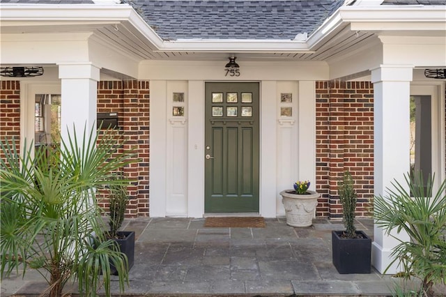 doorway to property with brick siding and a shingled roof