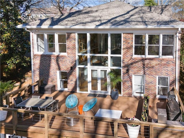 back of house with brick siding, french doors, a wooden deck, and roof with shingles