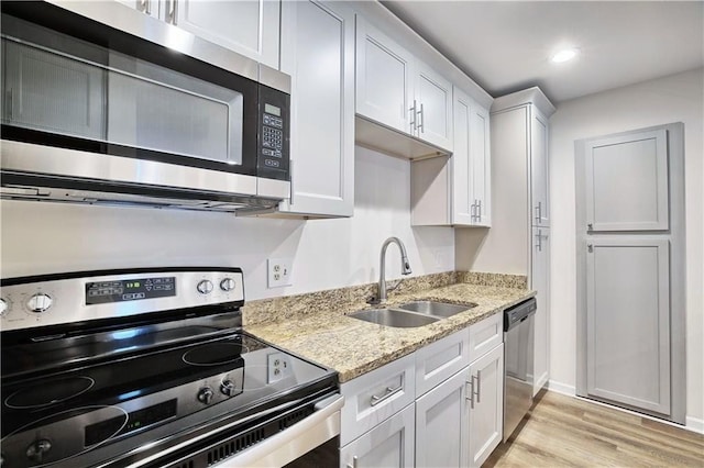 kitchen featuring stainless steel appliances, a sink, white cabinetry, light wood-type flooring, and light stone countertops