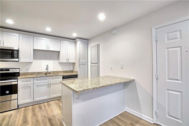 kitchen featuring light wood finished floors, appliances with stainless steel finishes, light stone countertops, a sink, and recessed lighting