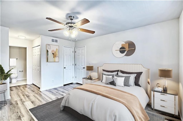 bedroom with wood finished floors, visible vents, multiple closets, baseboards, and ensuite bath