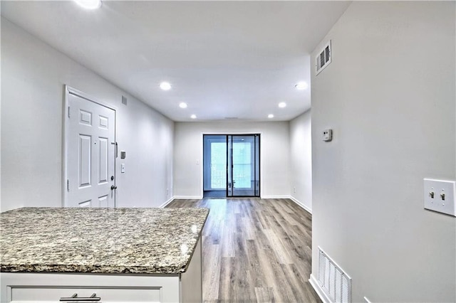 interior space with baseboards, visible vents, light stone countertops, light wood-type flooring, and white cabinetry