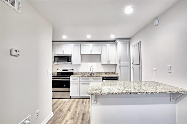 kitchen featuring light wood-style flooring, a sink, visible vents, appliances with stainless steel finishes, and light stone countertops