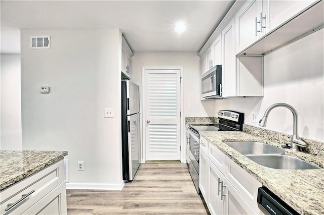 kitchen featuring light stone counters, light wood-style flooring, a sink, visible vents, and appliances with stainless steel finishes