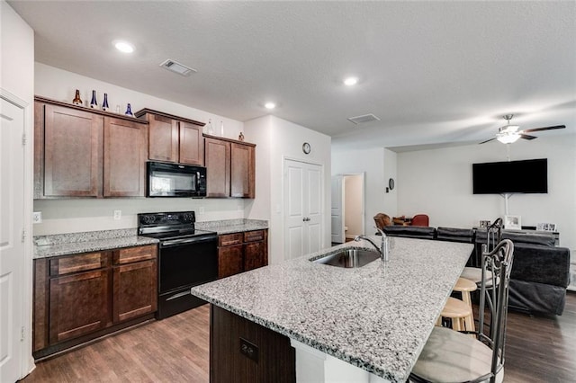 kitchen with sink, an island with sink, black appliances, and hardwood / wood-style flooring