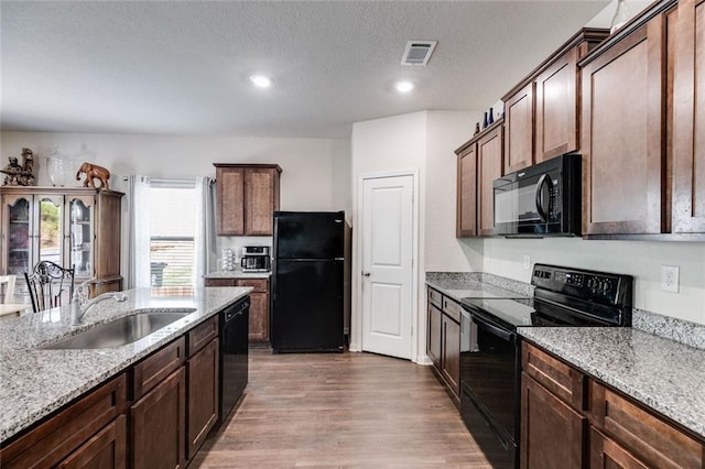 kitchen featuring sink, light stone counters, light hardwood / wood-style floors, a textured ceiling, and black appliances