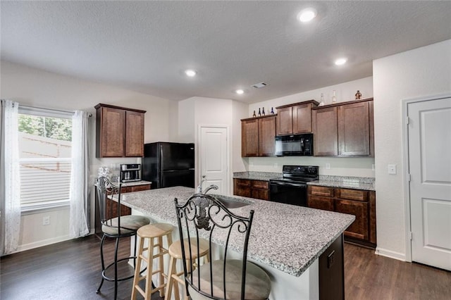 kitchen featuring light stone countertops, a center island with sink, black appliances, and sink