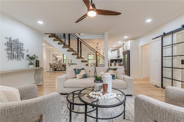 living room featuring ceiling fan, a barn door, and light hardwood / wood-style floors