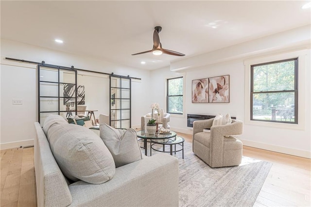 living room featuring light hardwood / wood-style floors, ceiling fan, and a barn door