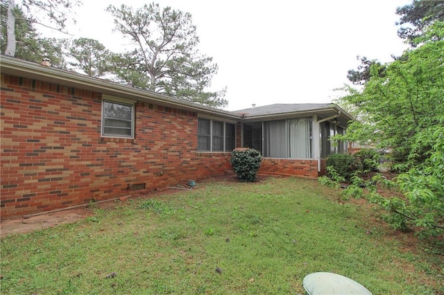 view of side of property featuring brick siding, a yard, and a sunroom