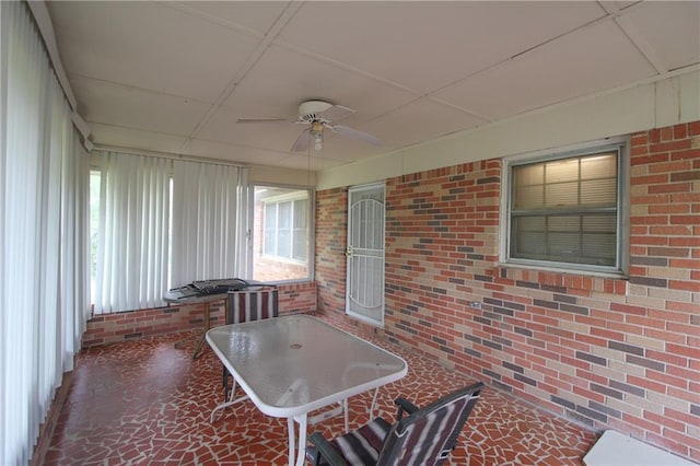 sunroom / solarium with brick wall, a ceiling fan, and a drop ceiling