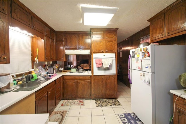 kitchen featuring a sink, white appliances, light tile patterned floors, light countertops, and under cabinet range hood