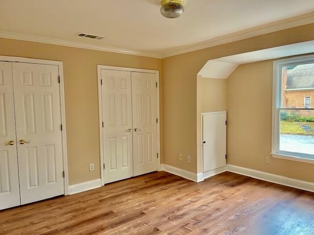 corridor with wood-type flooring, decorative columns, and crown molding