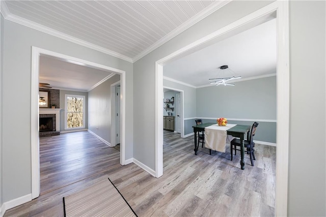 dining room featuring ornamental molding, a brick fireplace, wood finished floors, and baseboards