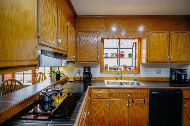 kitchen with a sink, black appliances, tile counters, under cabinet range hood, and brown cabinets