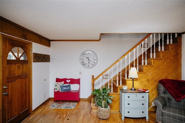 entrance foyer featuring a textured ceiling, wood finished floors, stairway, crown molding, and baseboards