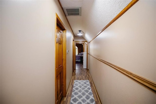 corridor with light wood finished floors, visible vents, a textured ceiling, and baseboards