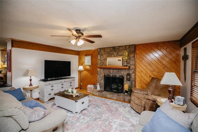 living area with a stone fireplace, wood walls, a textured ceiling, and ceiling fan