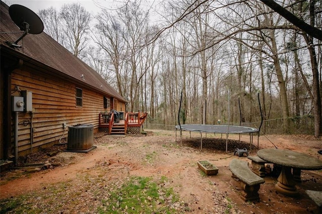 view of yard featuring a wooden deck, central air condition unit, a trampoline, and fence