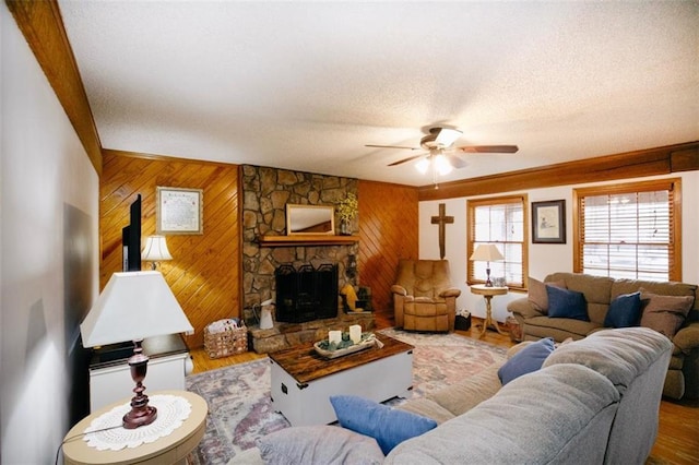 living room with a textured ceiling, wood finished floors, wooden walls, a stone fireplace, and ceiling fan