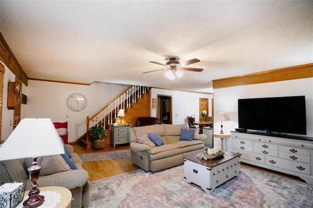 living room with ornamental molding, a textured ceiling, wood finished floors, stairway, and ceiling fan