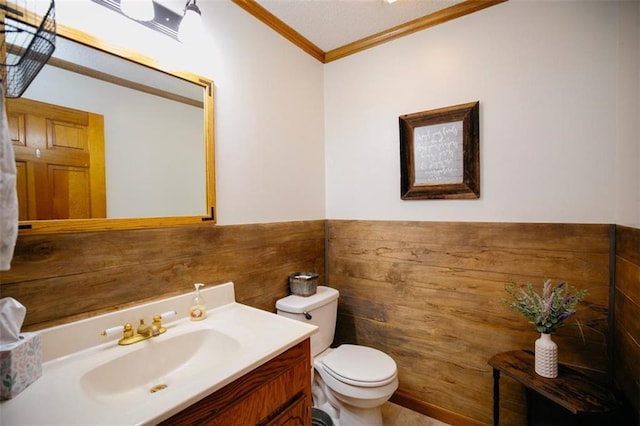 bathroom featuring wooden walls, crown molding, a wainscoted wall, toilet, and vanity