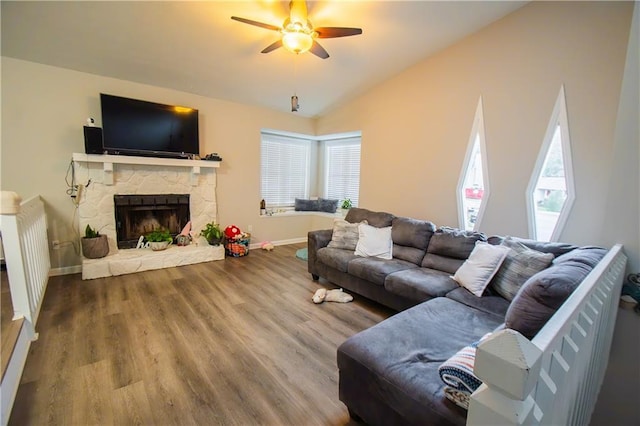 living area with a healthy amount of sunlight, vaulted ceiling, wood finished floors, and a stone fireplace