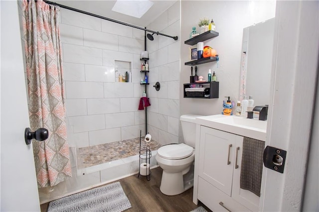 bathroom with toilet, a skylight, wood finished floors, vanity, and a shower stall