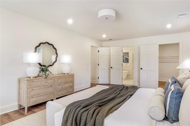 bedroom featuring visible vents, a spacious closet, ensuite bath, wood finished floors, and baseboards