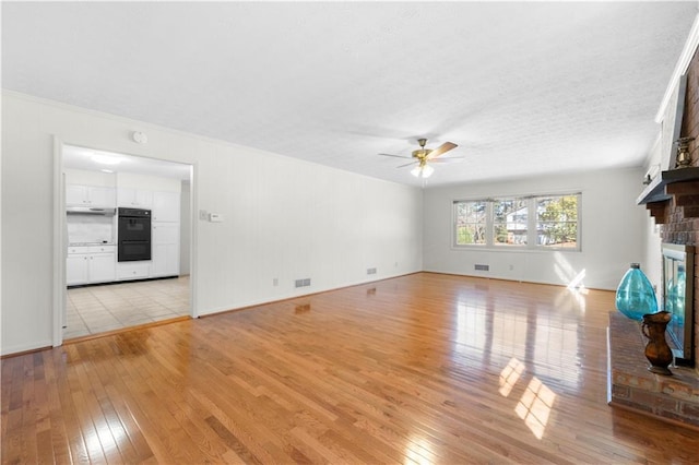 unfurnished living room featuring visible vents, a fireplace, a ceiling fan, and light wood-style floors