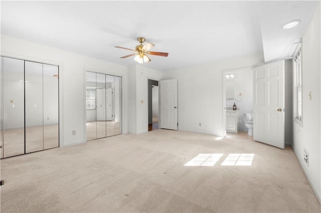 unfurnished bedroom featuring ensuite bath, a ceiling fan, multiple closets, and carpet flooring