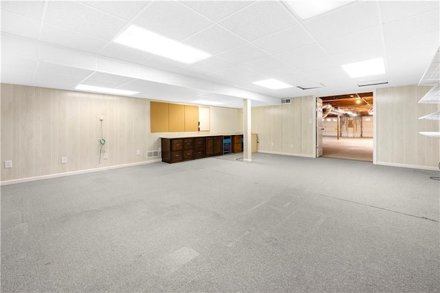 finished below grade area featuring a paneled ceiling, wood walls, baseboards, and carpet flooring