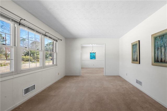 empty room featuring light colored carpet, visible vents, a textured ceiling, and baseboards