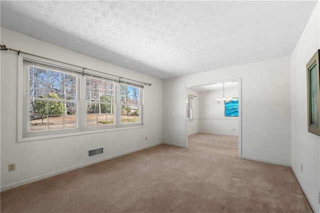 carpeted spare room with a chandelier, a textured ceiling, visible vents, and baseboards