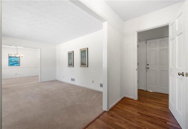 carpeted empty room with baseboards, wood finished floors, visible vents, and a notable chandelier