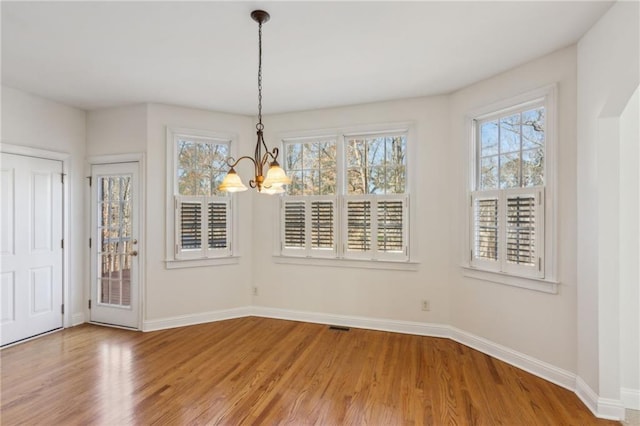 unfurnished dining area featuring light wood-style floors, a chandelier, and baseboards