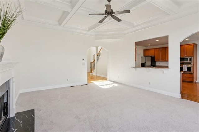 unfurnished living room with arched walkways, coffered ceiling, a fireplace, and stairway