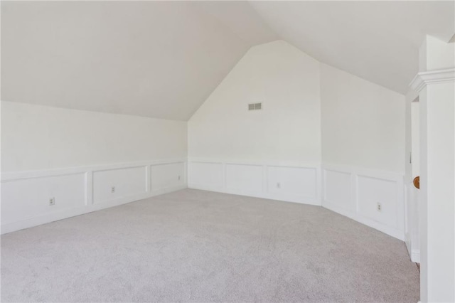 additional living space with vaulted ceiling, light carpet, visible vents, and a decorative wall