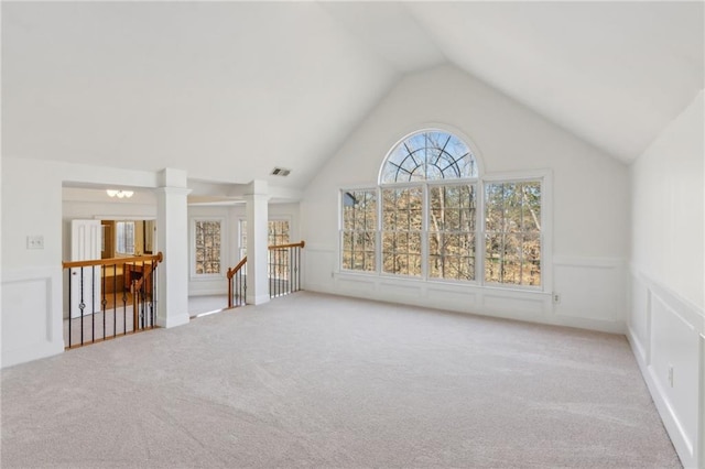 unfurnished living room with lofted ceiling, carpet flooring, visible vents, and ornate columns