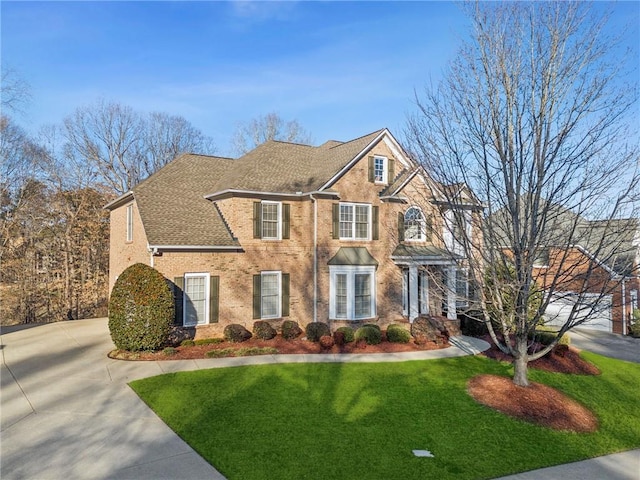 view of front of house featuring brick siding, a shingled roof, a front yard, a garage, and driveway